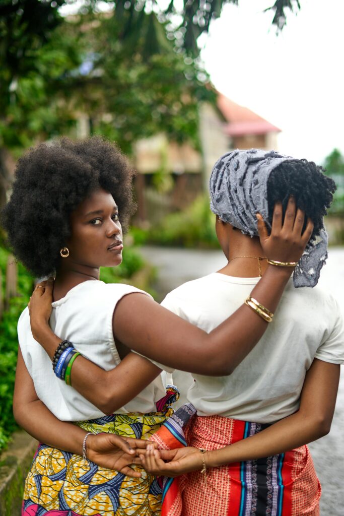 Two women standing outdoors embracing each other, dressed in colorful patterned skirts, symbolizing friendship, connection, and cultural identity.